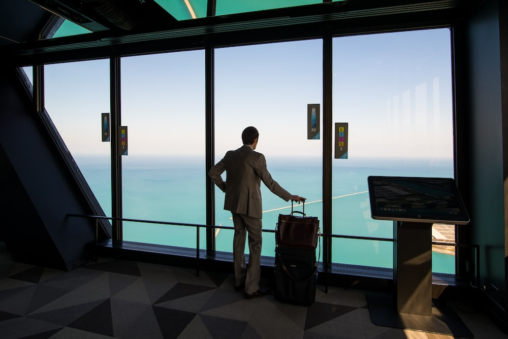 a person looking out a window while holding his luggage