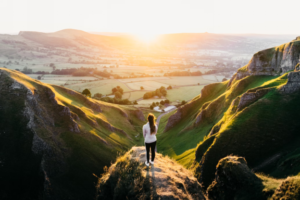 A photo showing a woman standing on a hill overlooking fields.