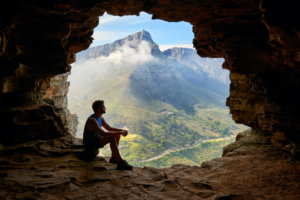 A photo showing a man sitting at the edge of a cave.