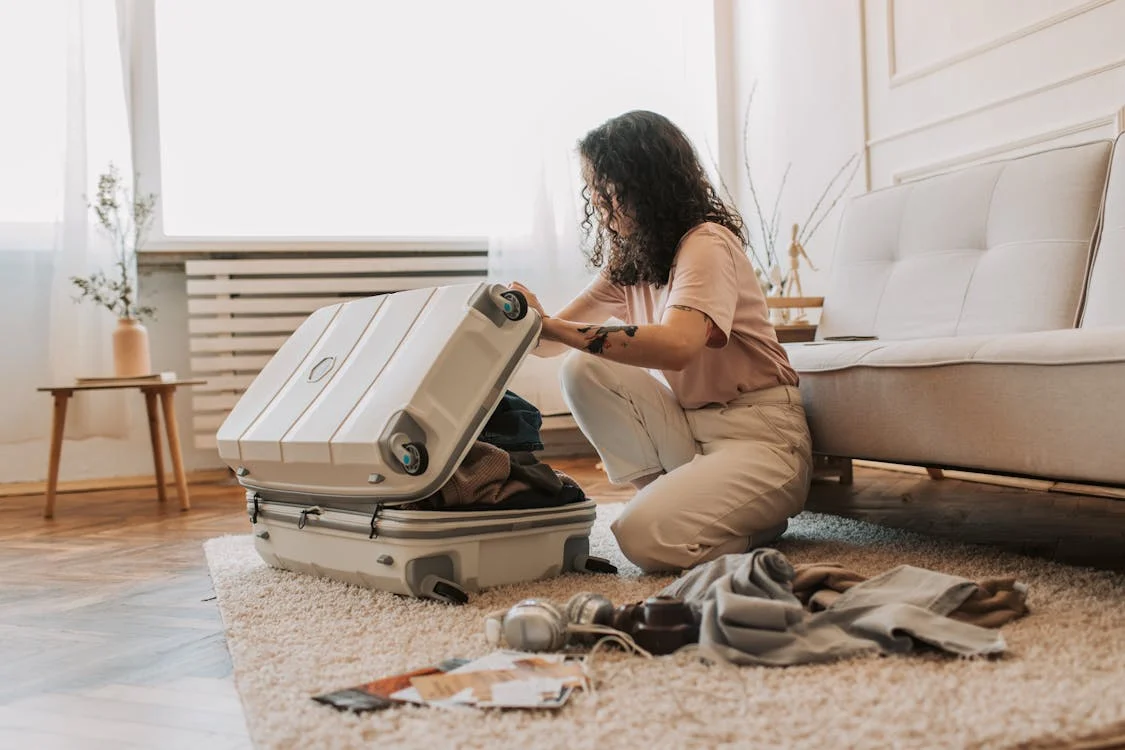 A woman urgently packing a suitcase with travel documents on top.