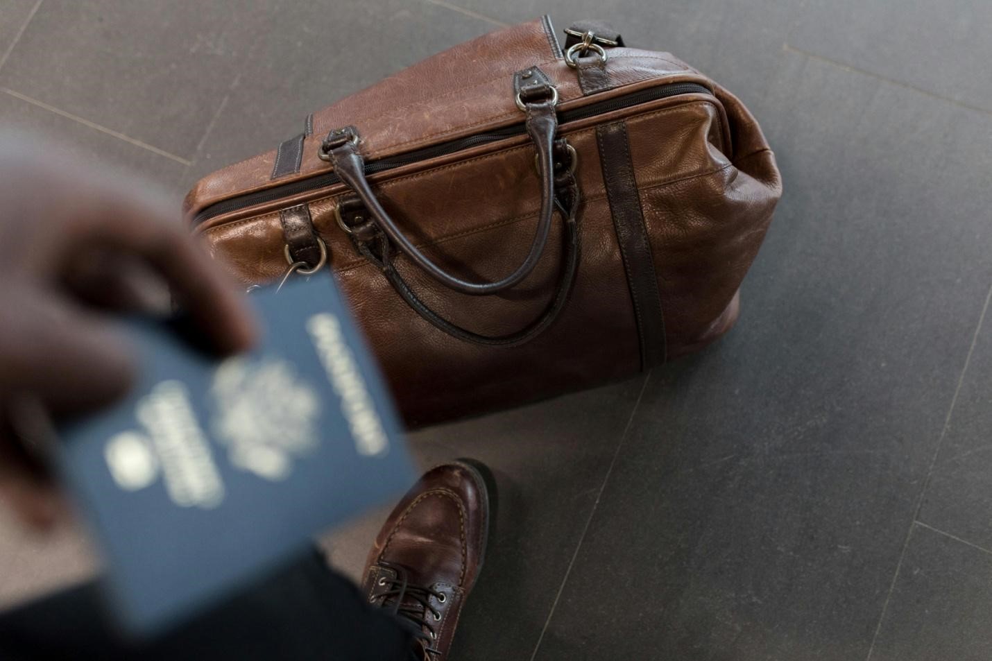 A picture of a person holding a passport with a travel bag placed on the floor